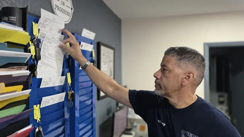 Anthony Pujols pulling a repair order from the shop's work board, keys and folders lined up beside it