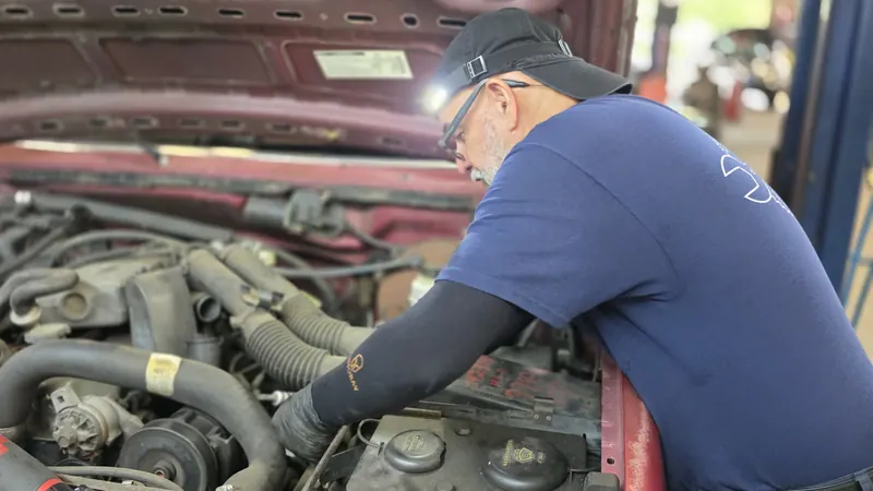 A technician with a headlamp leaning into an engine bay at Oviedo Car Care, tracing a problem