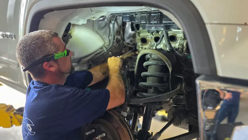 An Oviedo Car Care technician working on a vehicle's front suspension with the wheel removed