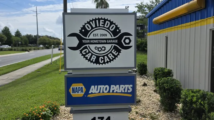 The Oviedo Car Care road sign on Mitchell Hammock Road with the NAPA Auto Parts sign directly below it