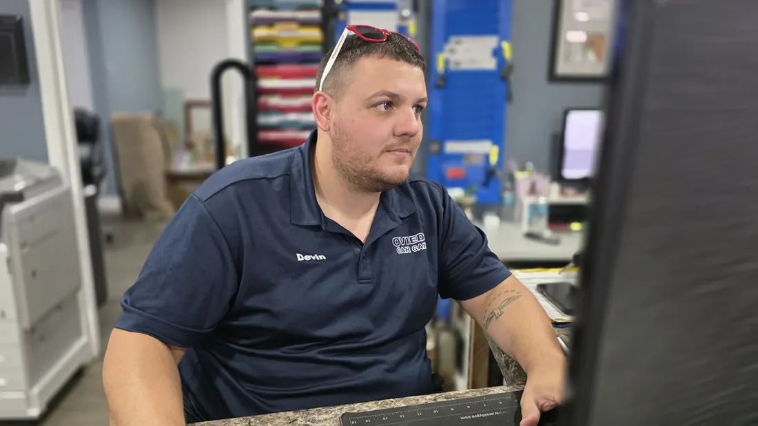 Devin at the front desk at Oviedo Car Care, sunglasses on his head, checking a repair order