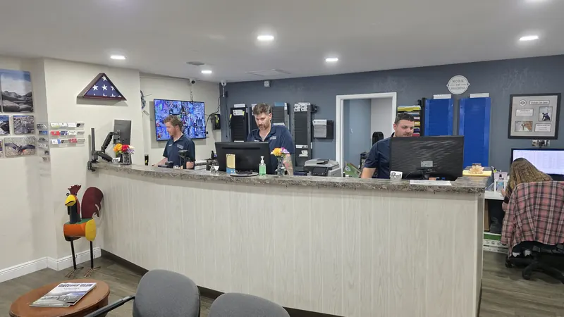 The Oviedo Car Care front desk with three service advisors helping customers — and the shop's metal rooster statue standing by the counter