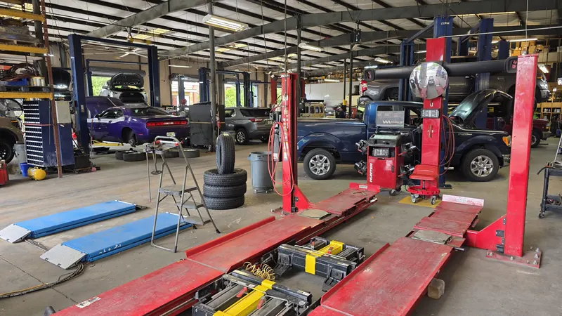 Inside the Oviedo Car Care shop: the red in-house alignment rack with the alignment computer beside it, a stack of new tires ready to mount, and cars up on lifts in the background